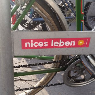 Ein Sticker mit der Aufschrift 'nices Leben' auf einem Fahrradständer.
