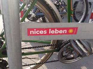 Ein Sticker mit der Aufschrift 'nices Leben' auf einem Fahrradständer.
